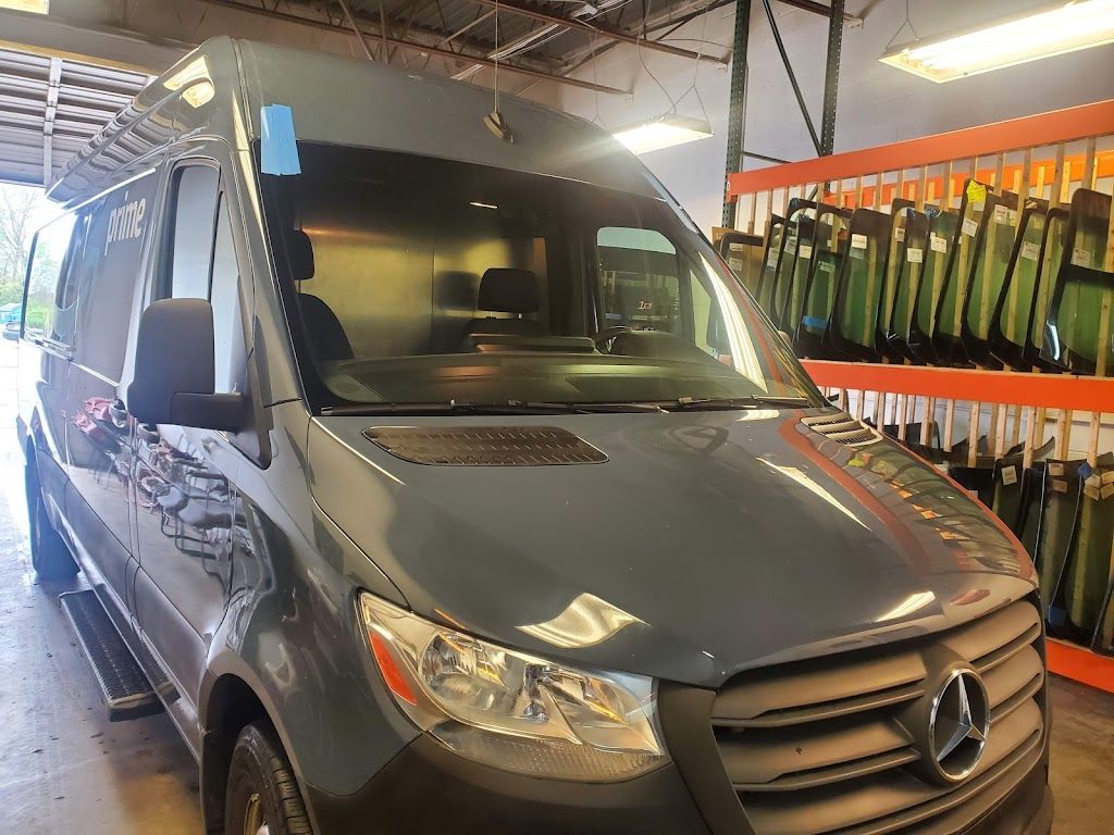A mercedes sprinter van is parked in a garage next to a rack of windshields.