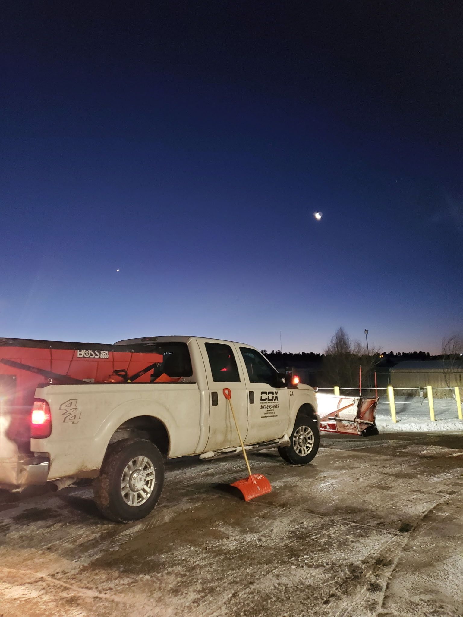 White pickup truck with snowplow attachment parked under a dark blue sky with a crescent moon.