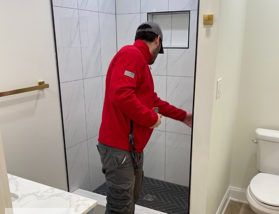 Man in red jacket, inspecting a newly tiled shower in a bathroom.
