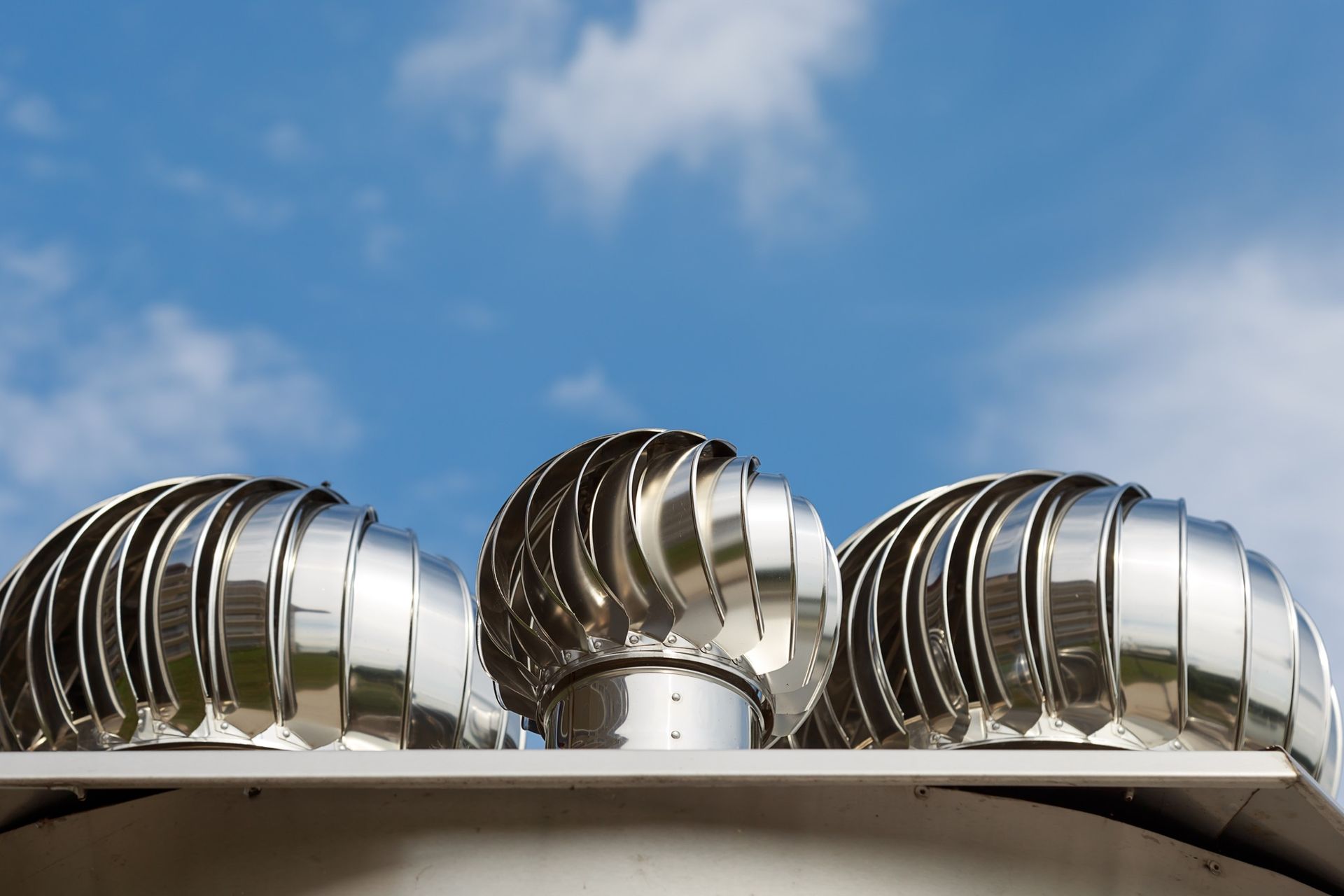 Three metallic roof turbine vents against a blue sky with white clouds.