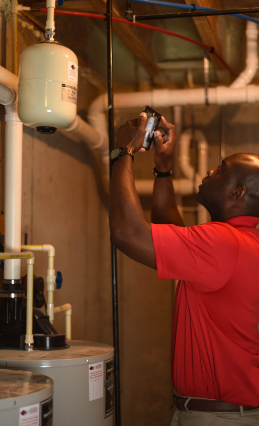 Man in red shirt taking a picture of a water heater in a basement setting.
