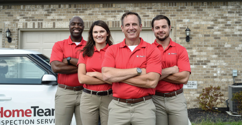 HomeTeam Inspection Services team in red shirts and khakis, arms crossed, smiling in front of a house.
