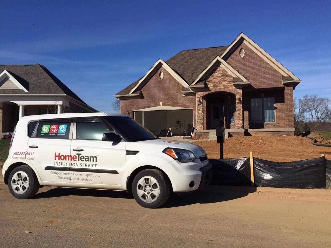 White car with HomeTeam logo parked in front of a brick house under construction on a sunny day.