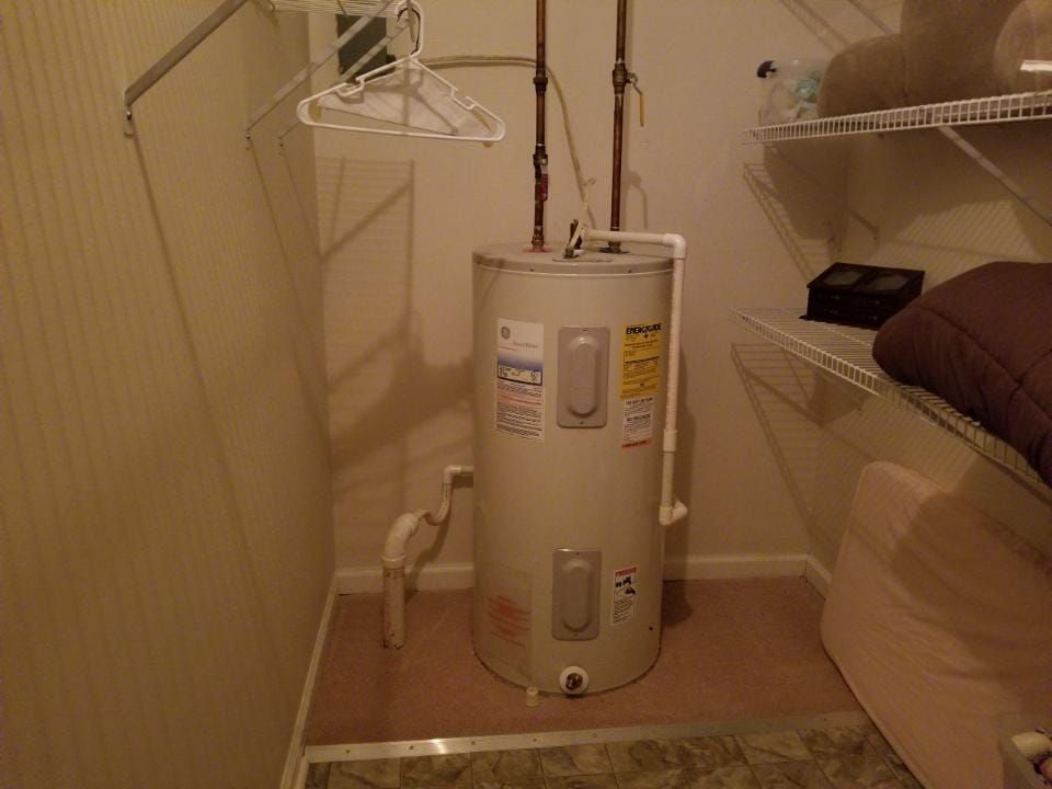 A water heater in a closet with shelves.