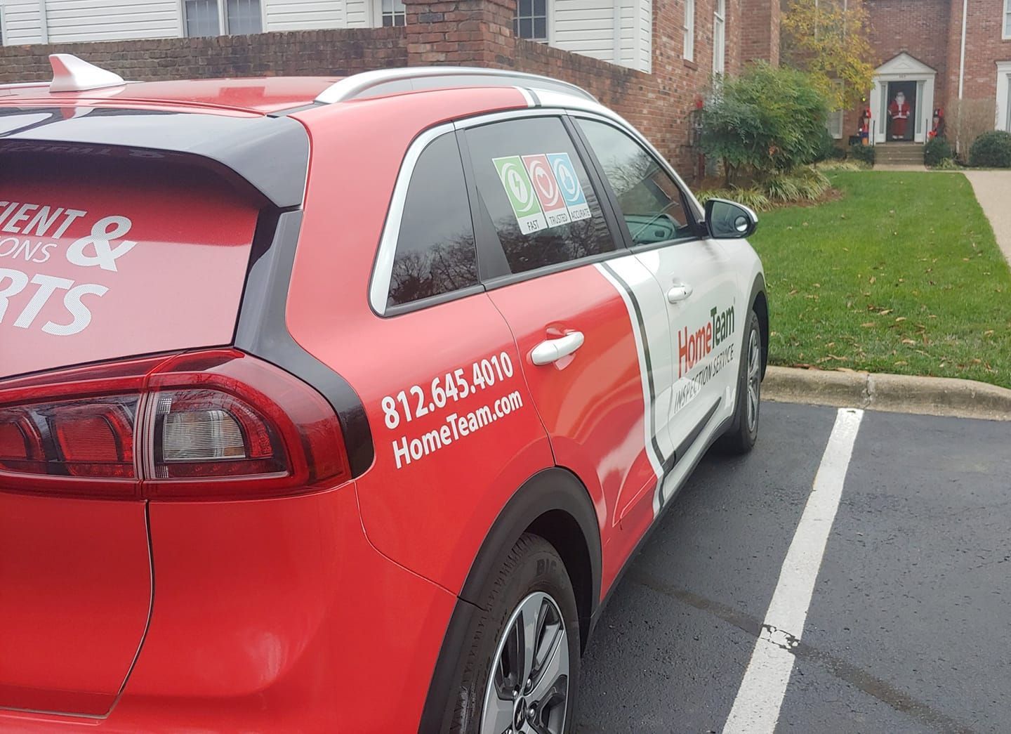 Red and white car parked, with company logo and phone number. In front of a building.