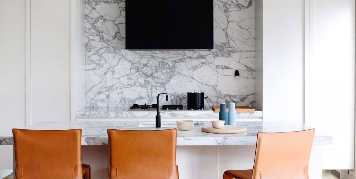 A modern kitchen with brown leather chairs, marble countertops, and a black range hood.