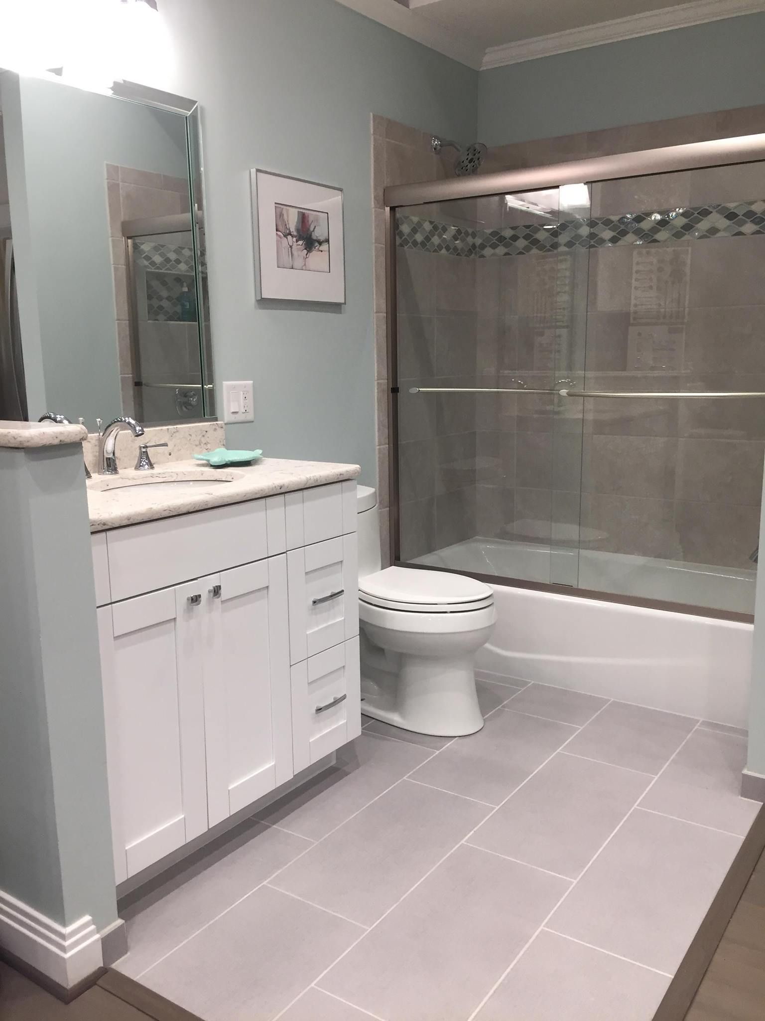 Bathroom with a white vanity, toilet, and shower. Gray floor tiles and blue-green walls.