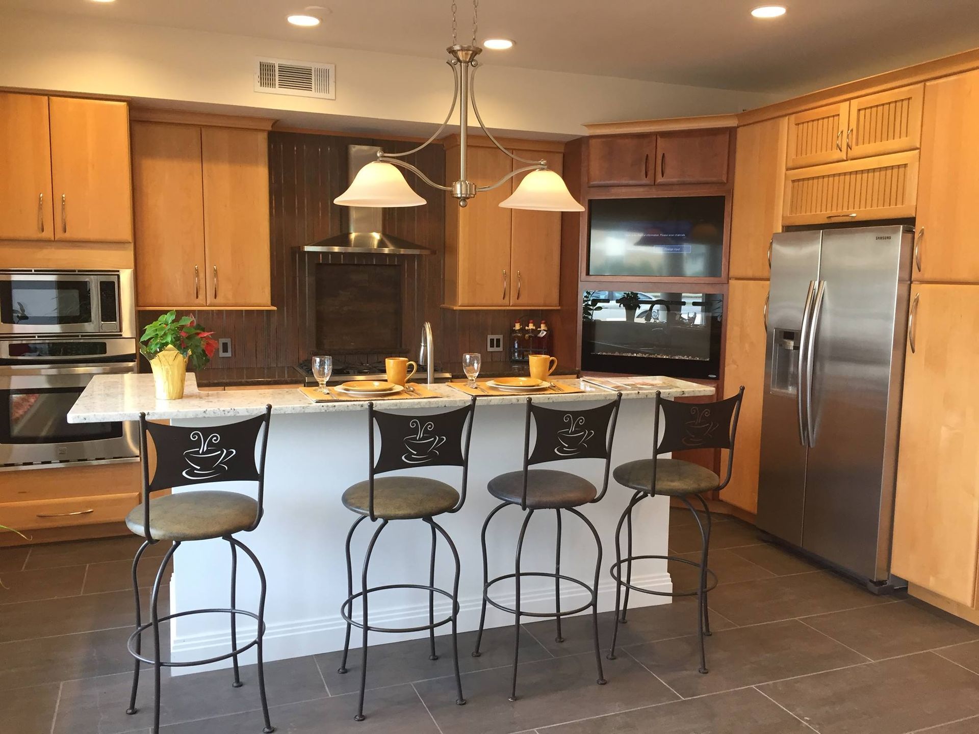 Kitchen with light wood cabinets, white island with four stools, stainless steel appliances.