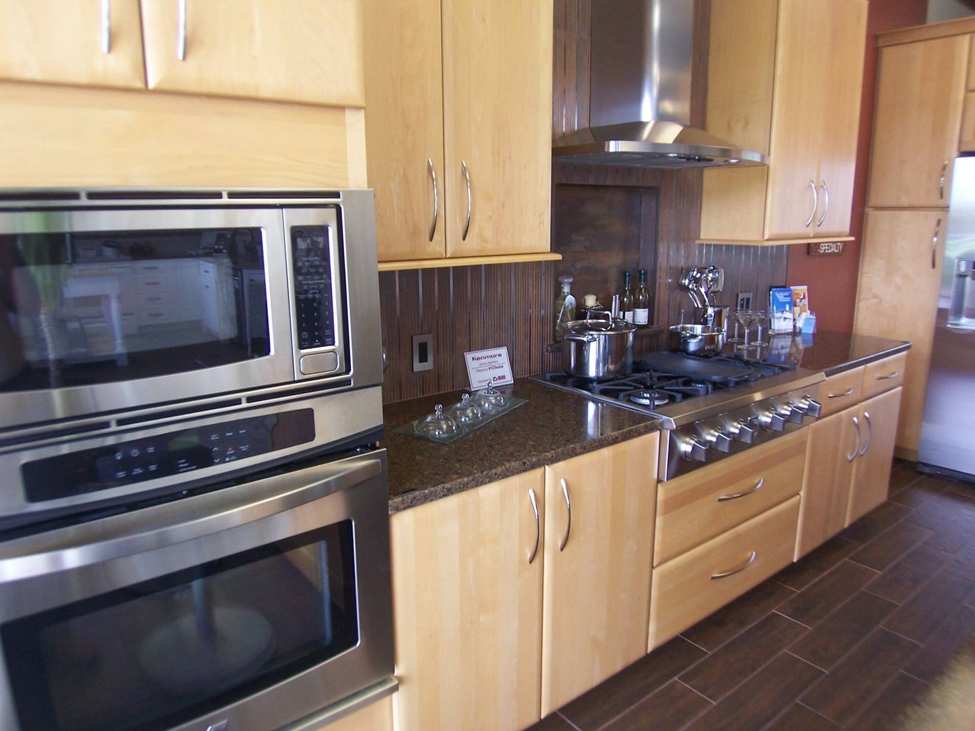 Modern kitchen with light wood cabinets, stainless steel appliances, and dark countertops.