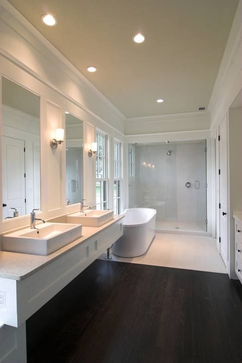 Modern white bathroom with dark wood floor, double vanity, freestanding tub, and shower.