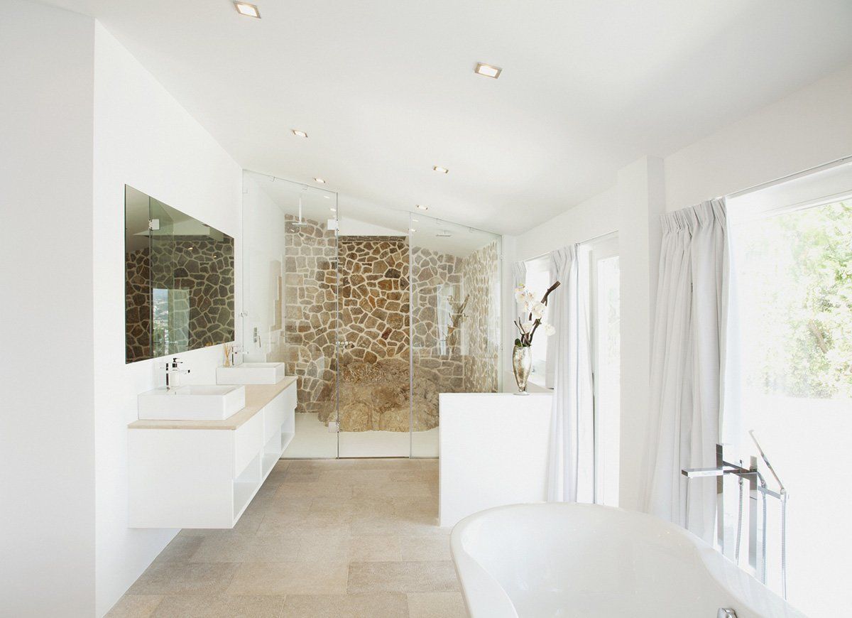 Bright white bathroom with stone shower, floating vanity, and a freestanding tub.