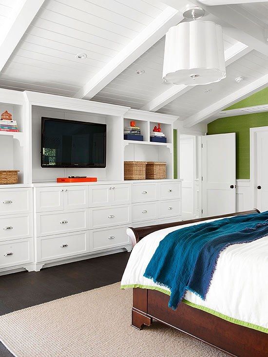 Bedroom with white built-in storage, TV, dark wood bed, and turquoise blanket. White vaulted ceiling, green accent wall.