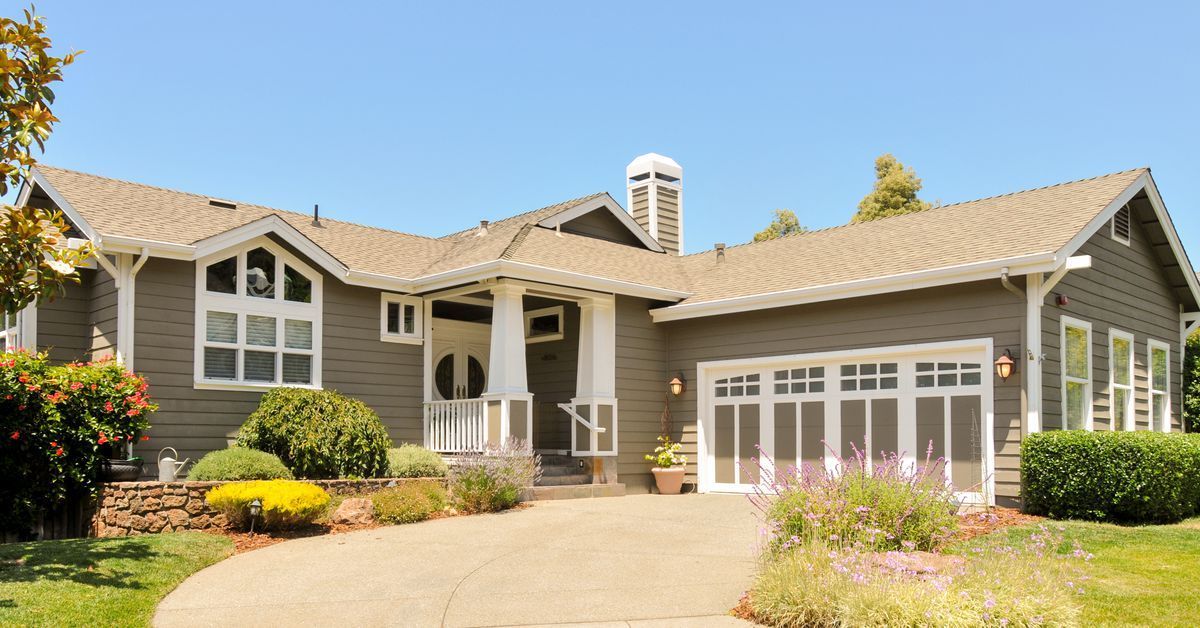 Gray house with a driveway and garden; white trim and a garage with a glass door.