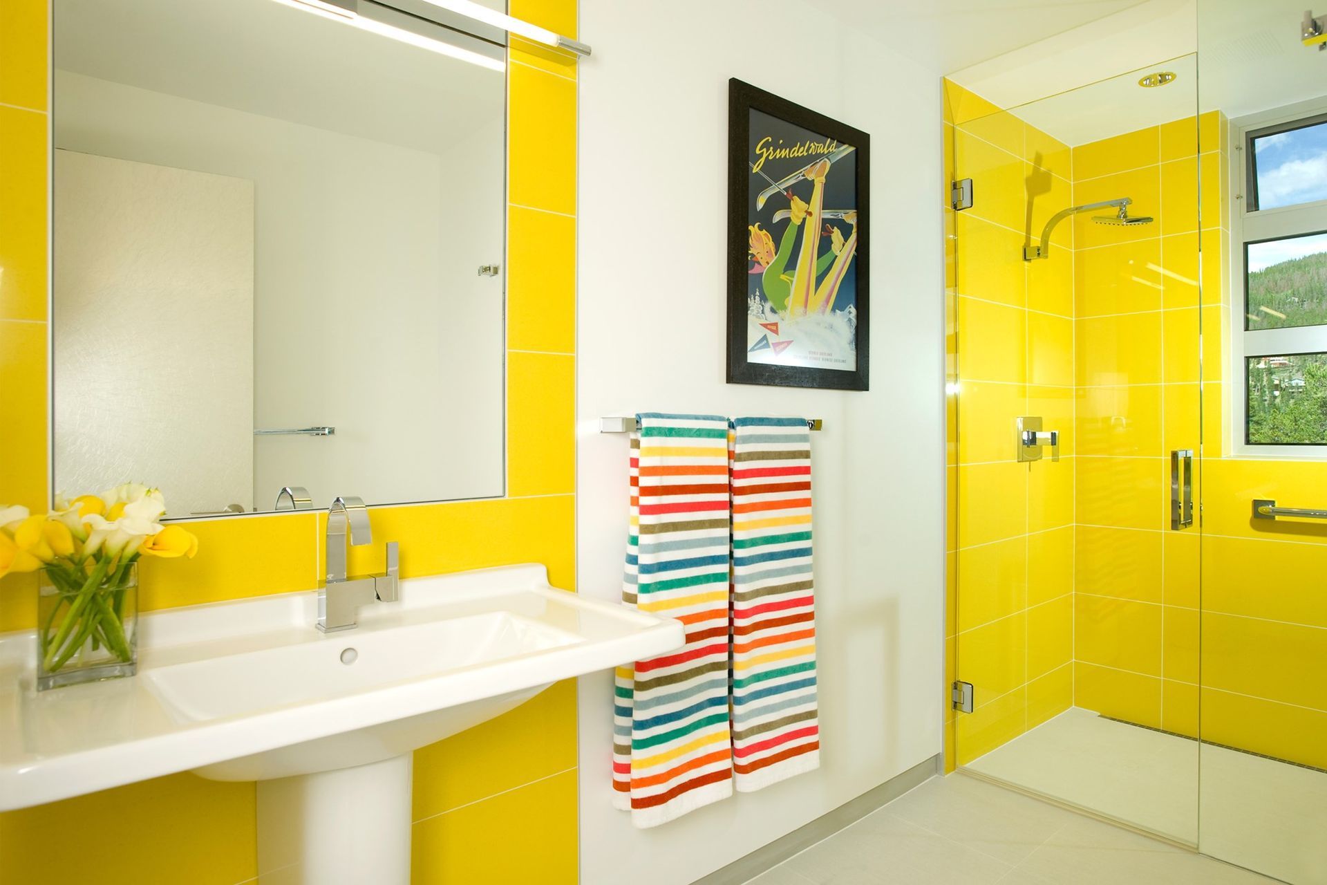 Yellow-tiled bathroom with a white sink, mirror, and shower. A colorful towel hangs on a rack.