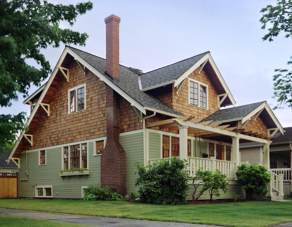 Two-story house with green siding, brown shingle siding, and a covered porch. Red brick chimney.
