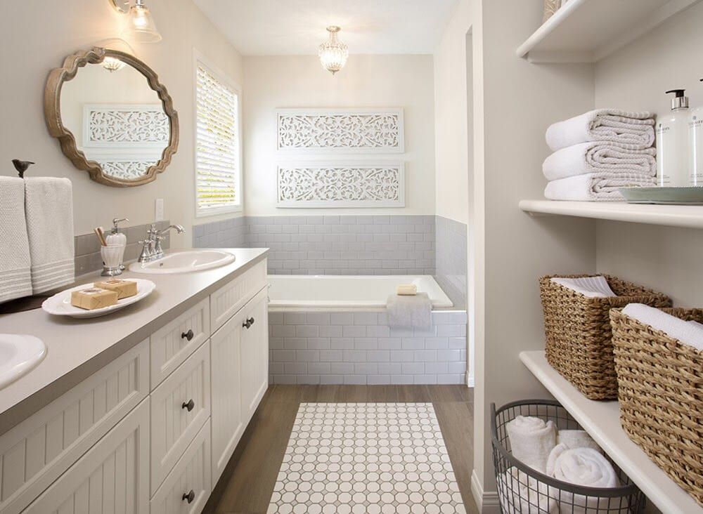 Bathroom with a white bathtub, gray cabinets, wicker baskets, and a decorative mirror.