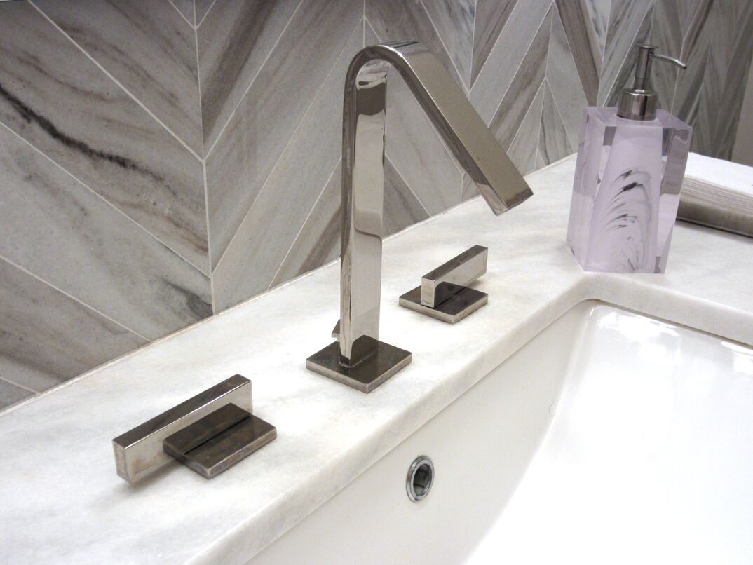 Modern bathroom faucet with two levers and a soap dispenser on a marble countertop.