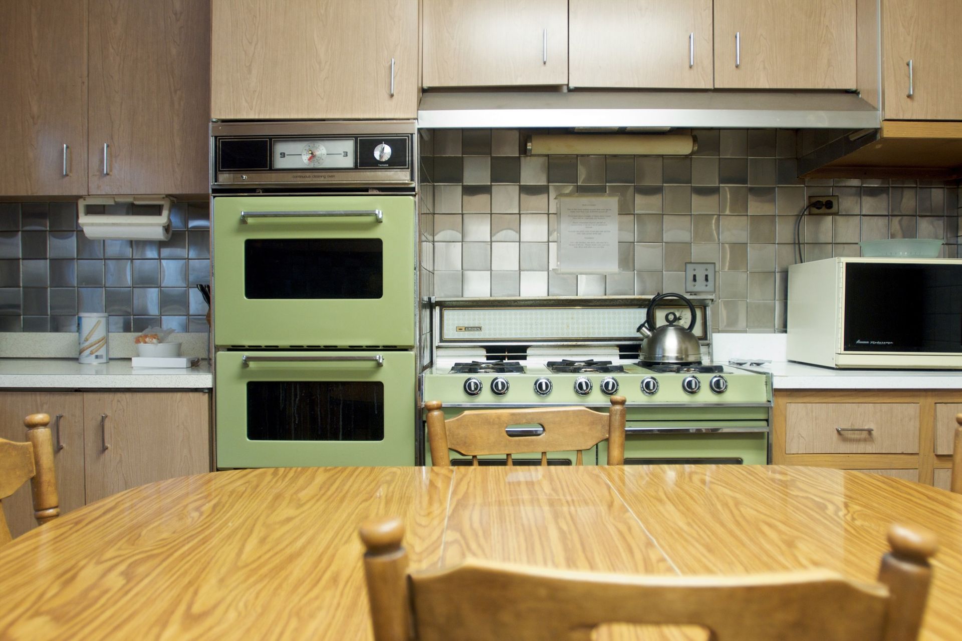A kitchen with a green stove and double oven, a microwave, and a wooden table with chairs.
