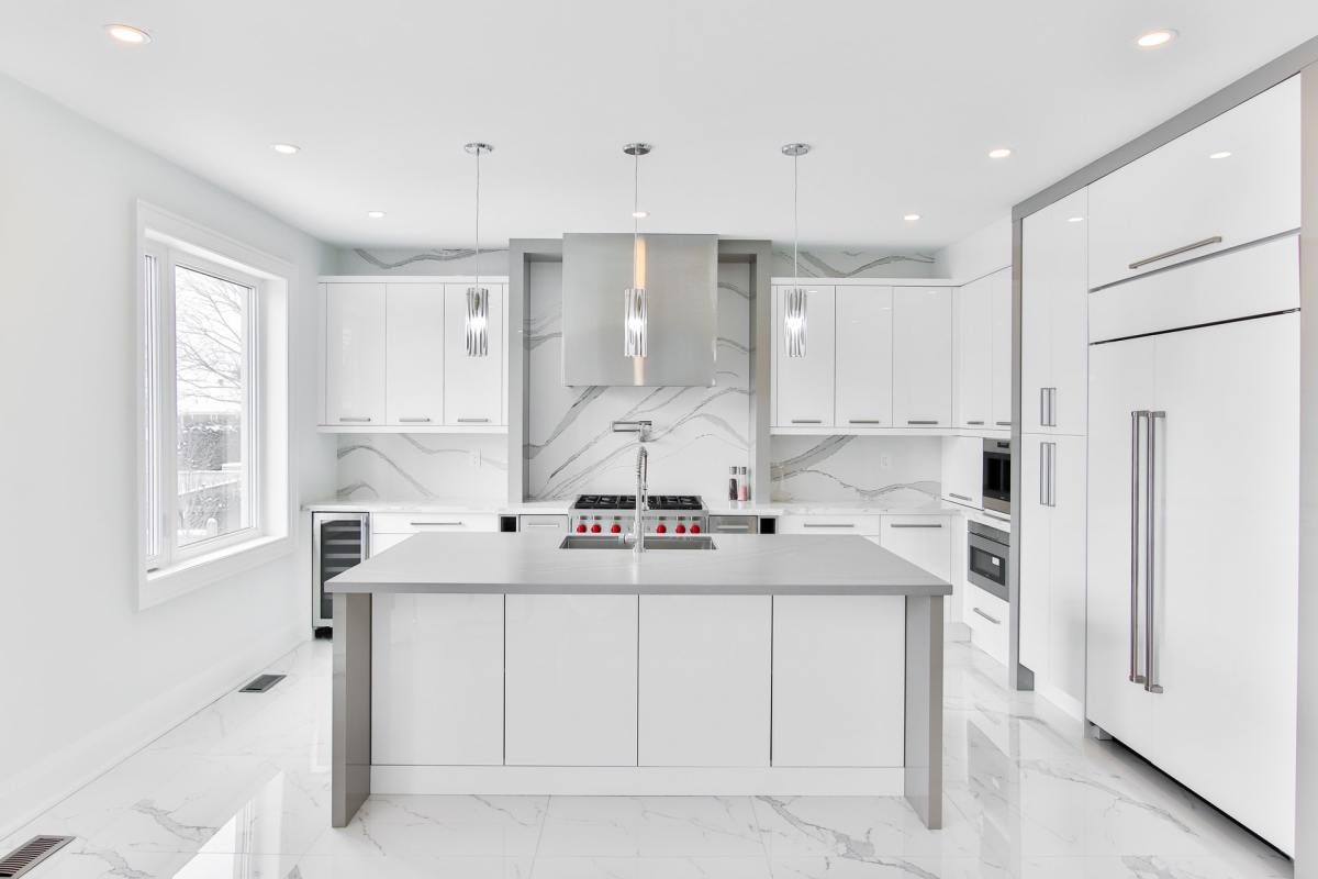Modern, all-white kitchen with marble backsplash, stainless steel appliances, and large island.
