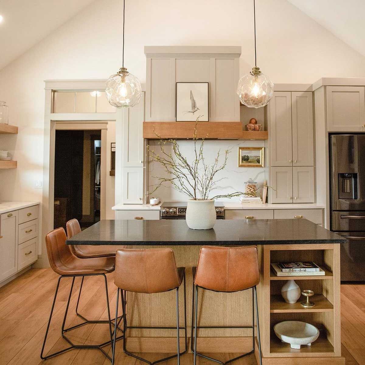 Modern kitchen with island, pendant lights, wooden shelves, and leather bar stools.