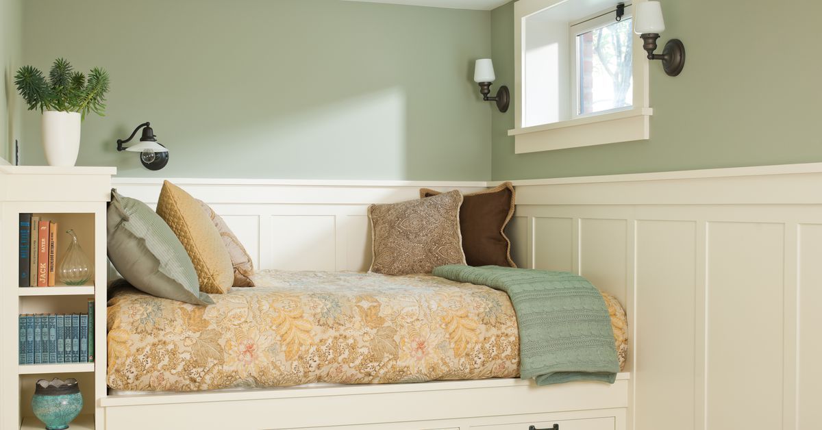 Cozy daybed nook with light green walls, cream wainscoting, and patterned bedding. Includes pillows, throw blanket, and wall sconces.