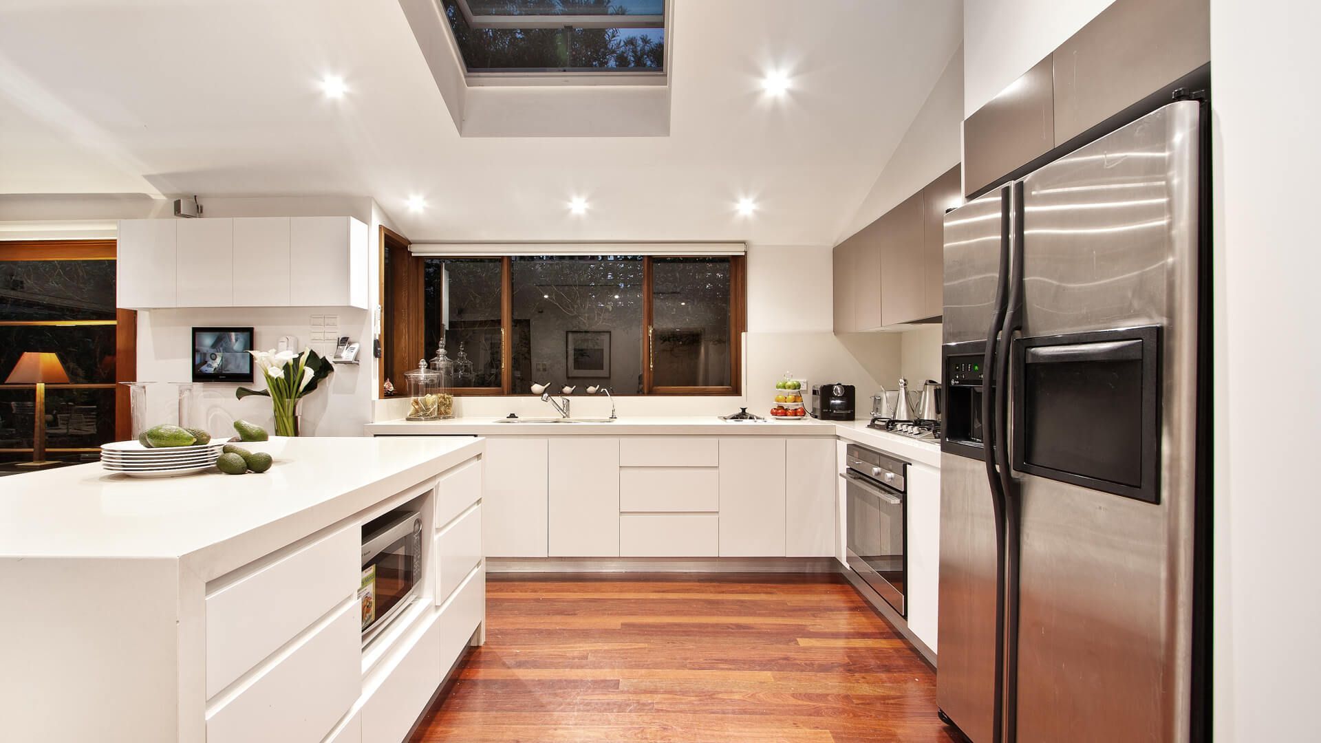 Modern kitchen with white cabinets, stainless steel appliances, and wooden floor.