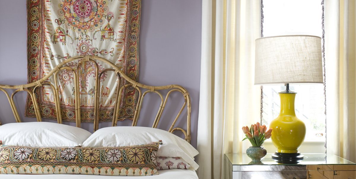 Bedroom with yellow lamp on nightstand, gold headboard, lavender wall.
