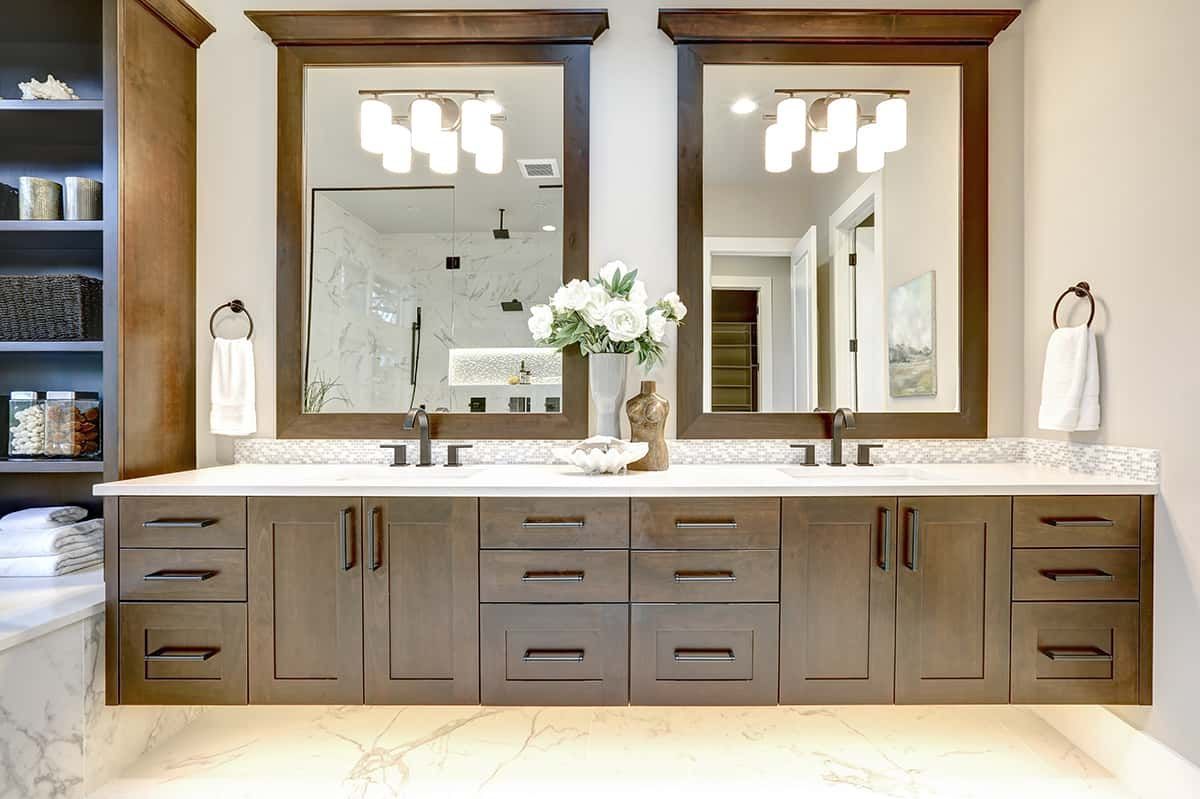 Bathroom with double vanity, two mirrors, and cabinets. Light gray walls, wooden trim, and marble floors.