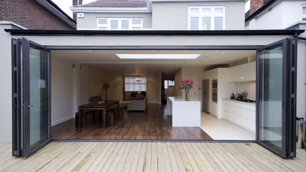 Open bi-fold doors reveal a modern kitchen and dining space with light wood floors and white walls.