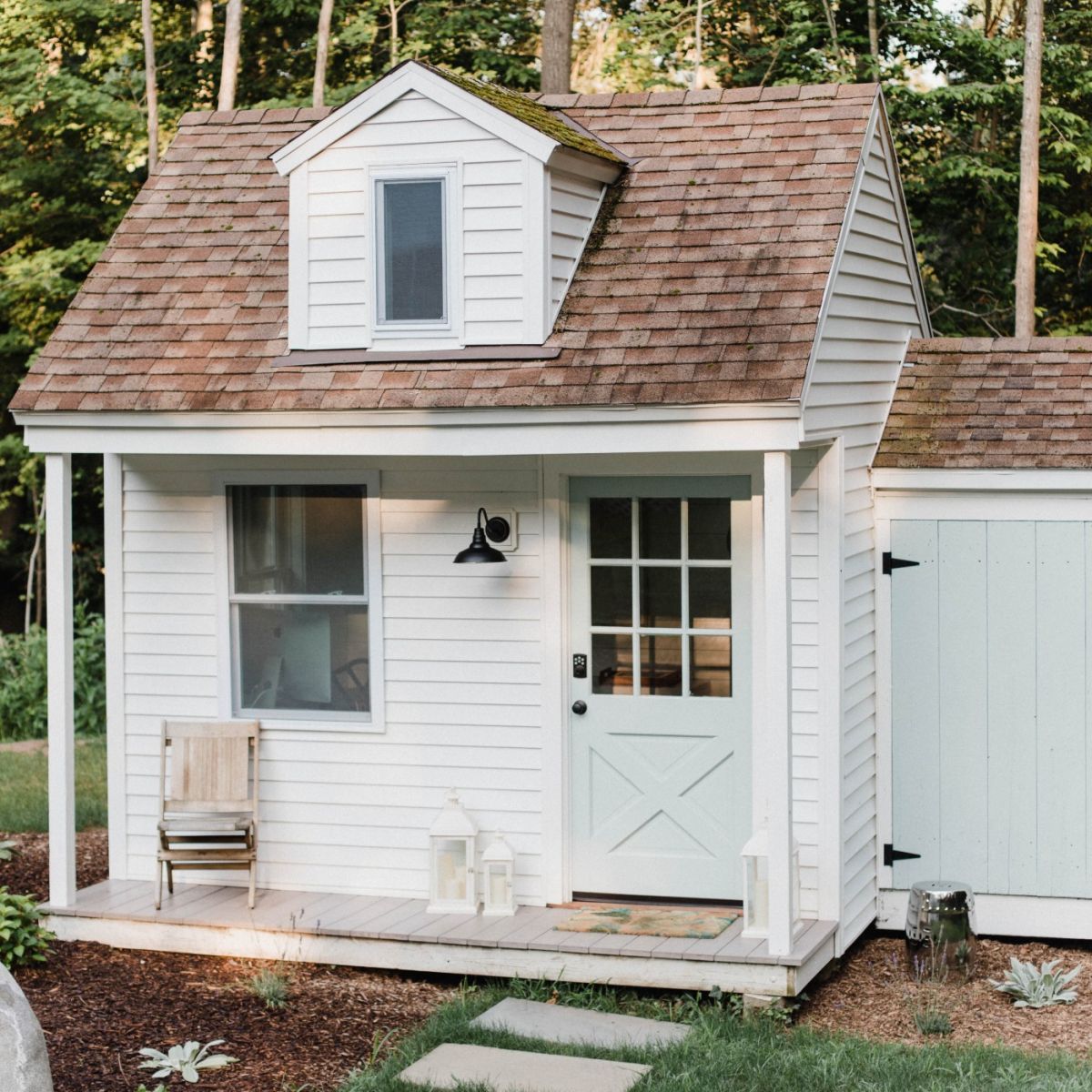 White cottage with a brown shingle roof, blue door, and small front porch.