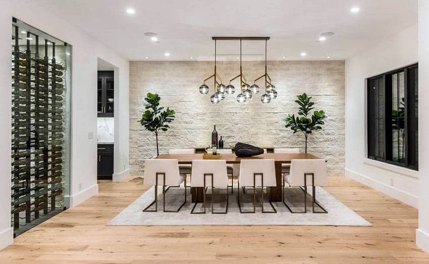 Dining room with wood table, white chairs, stone wall, and chandelier.