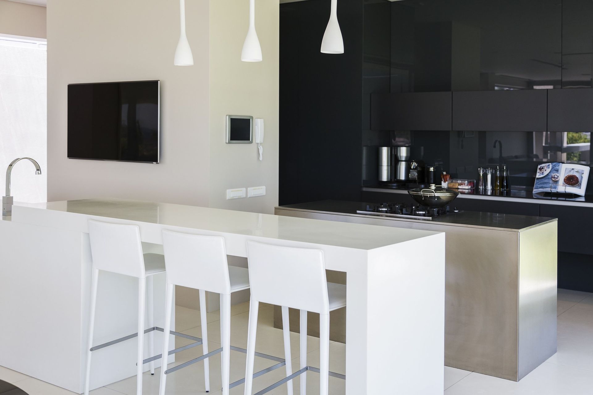 Modern kitchen with white island, stools, black cabinets, stainless steel accents, and hanging pendant lights.