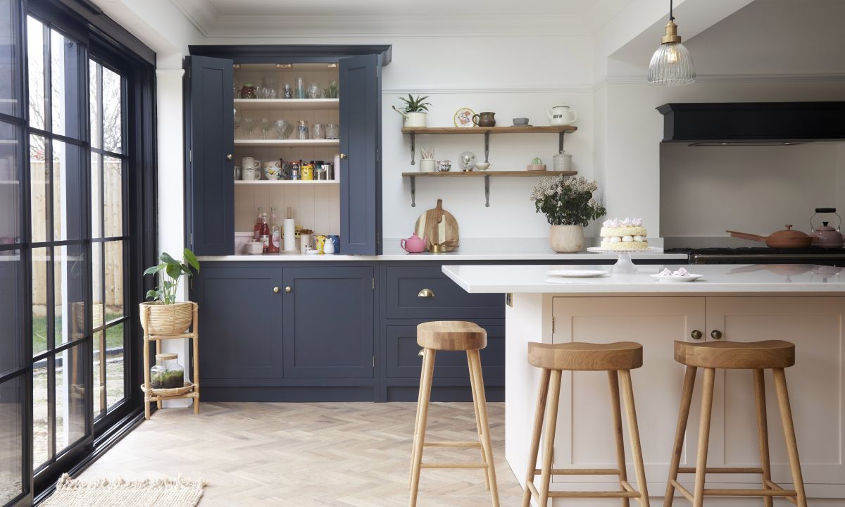 Kitchen with blue cabinets, white countertops, wooden stools, and large windows.
