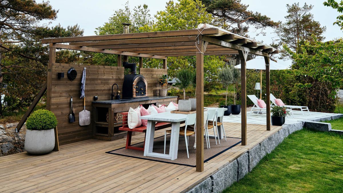 Outdoor kitchen with pizza oven, dining table, and pergola.