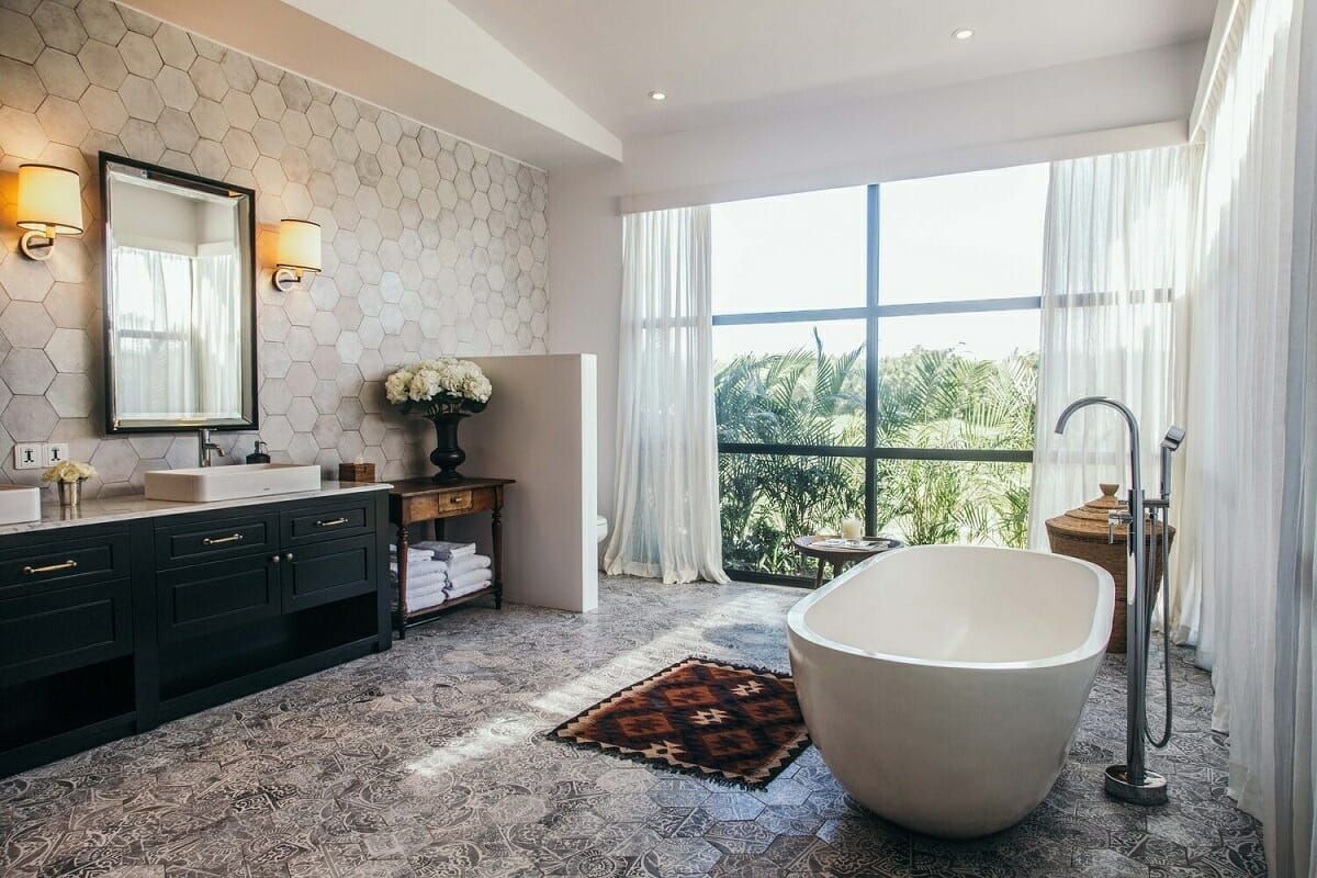 Luxurious bathroom with soaking tub, large window, dark vanity, and patterned floor.