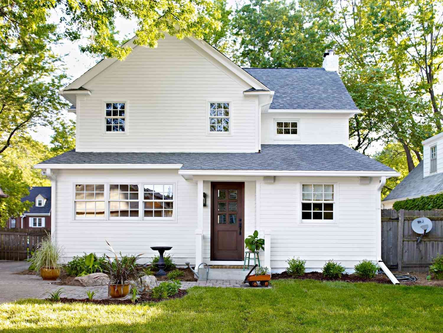 White two-story house with gray roof, brown door, and green lawn.