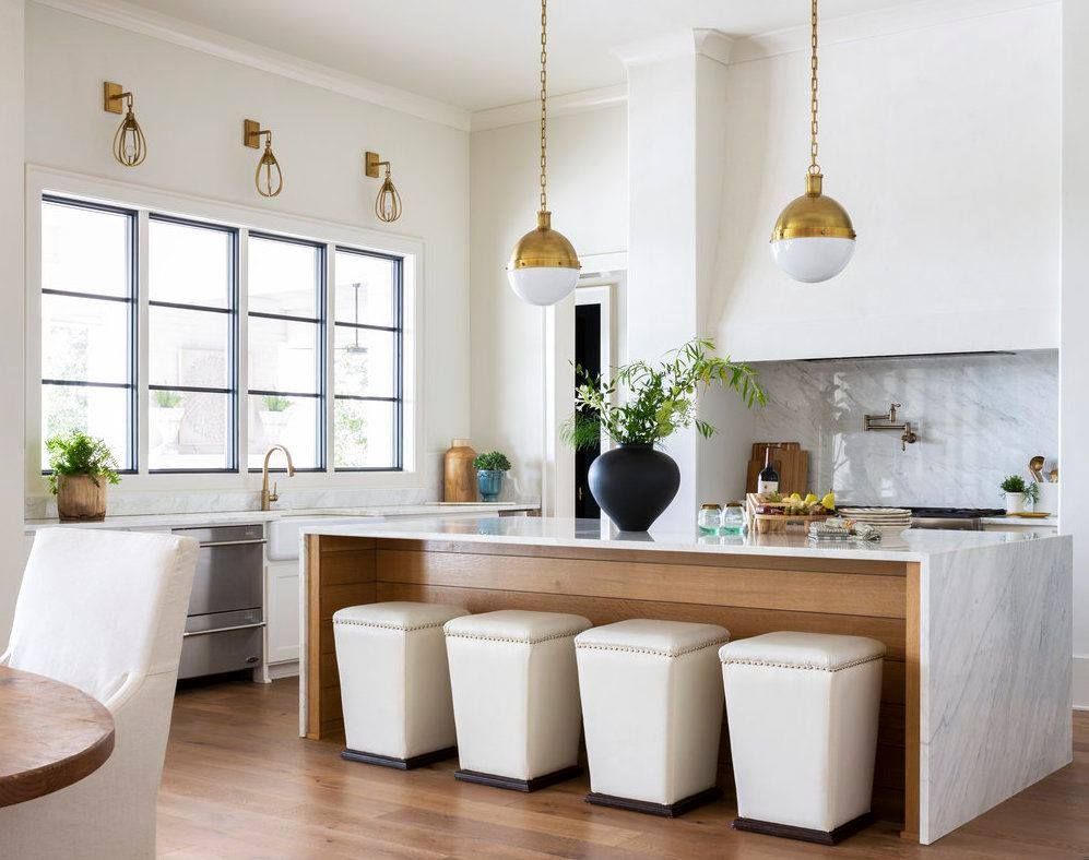 Bright kitchen with white island, gold light fixtures, and white stools.