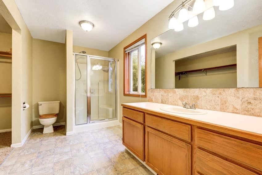 Bathroom with beige walls, a wood vanity, a shower, toilet, and window.