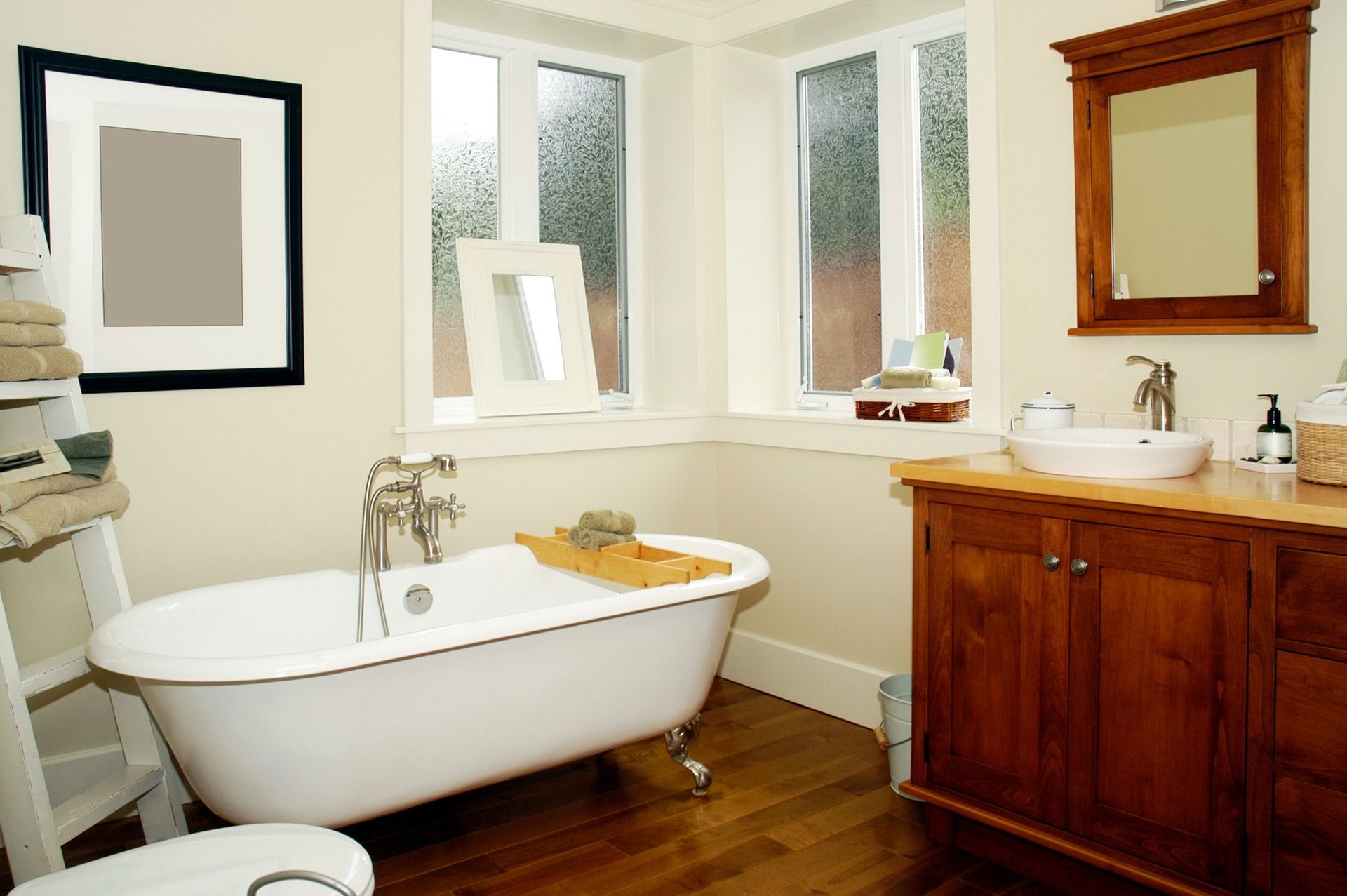 Bathroom with a claw-foot tub, vanity, and windows, with hardwood floors and light walls.