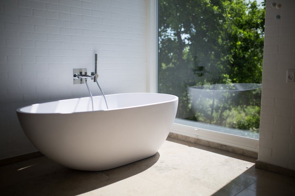 White oval bathtub by a large window overlooking trees.