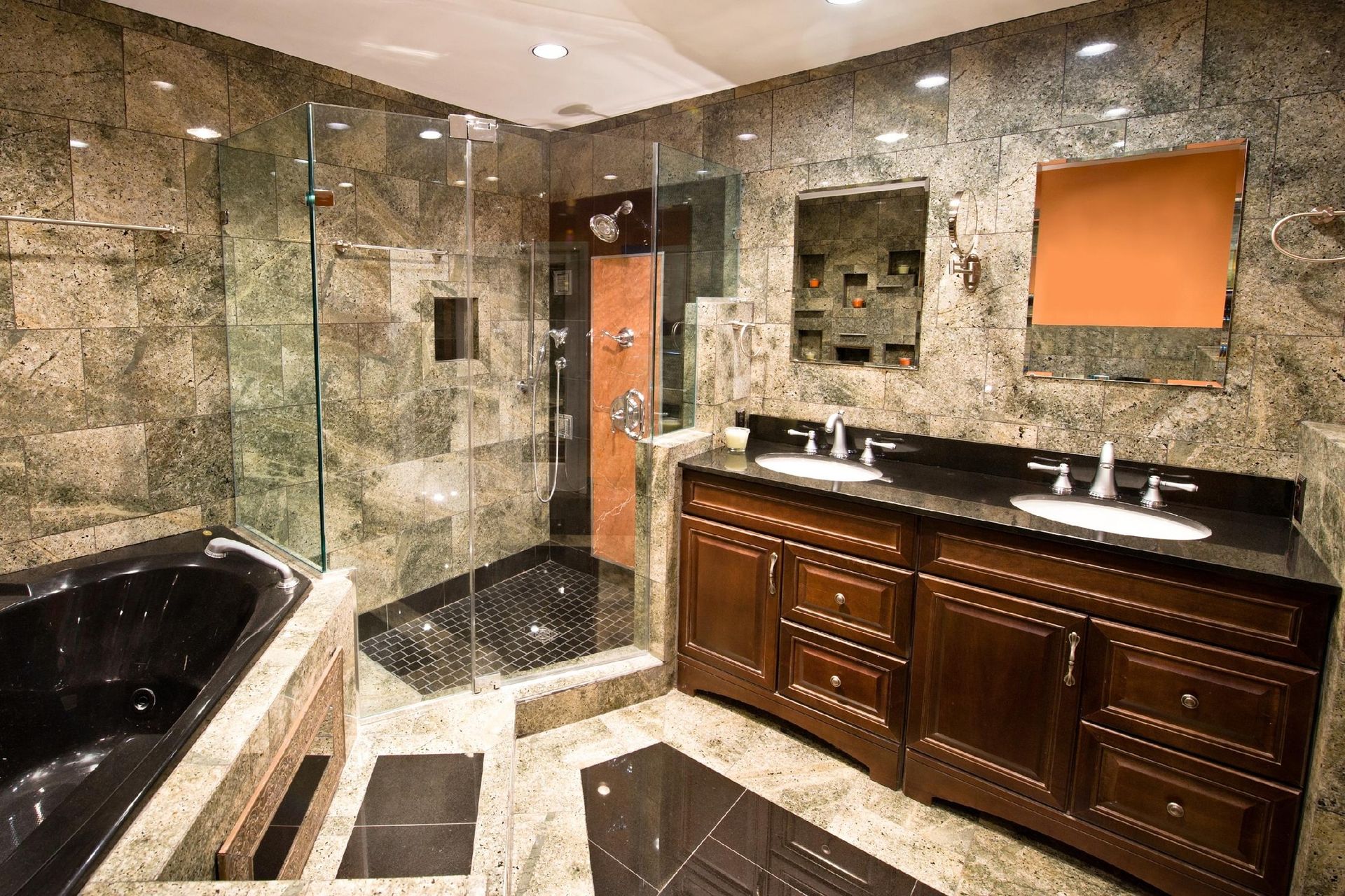 Luxurious bathroom with dark wood vanity, black countertops, marble walls, glass shower, and black bathtub.