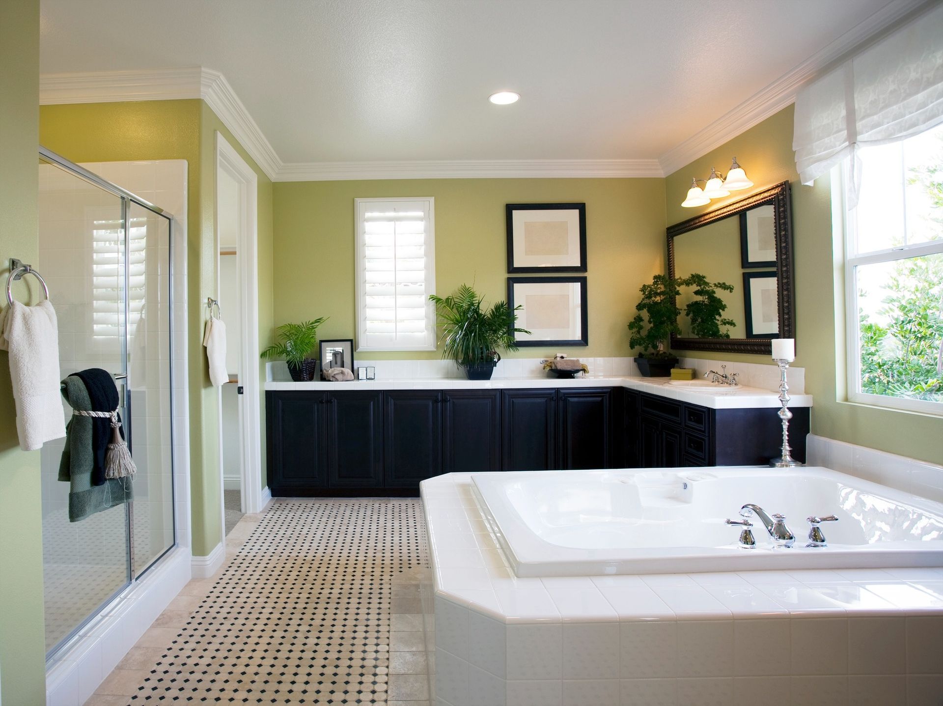 Spacious bathroom with white tub, black cabinets, and green walls. A shower and windows with bright daylight.