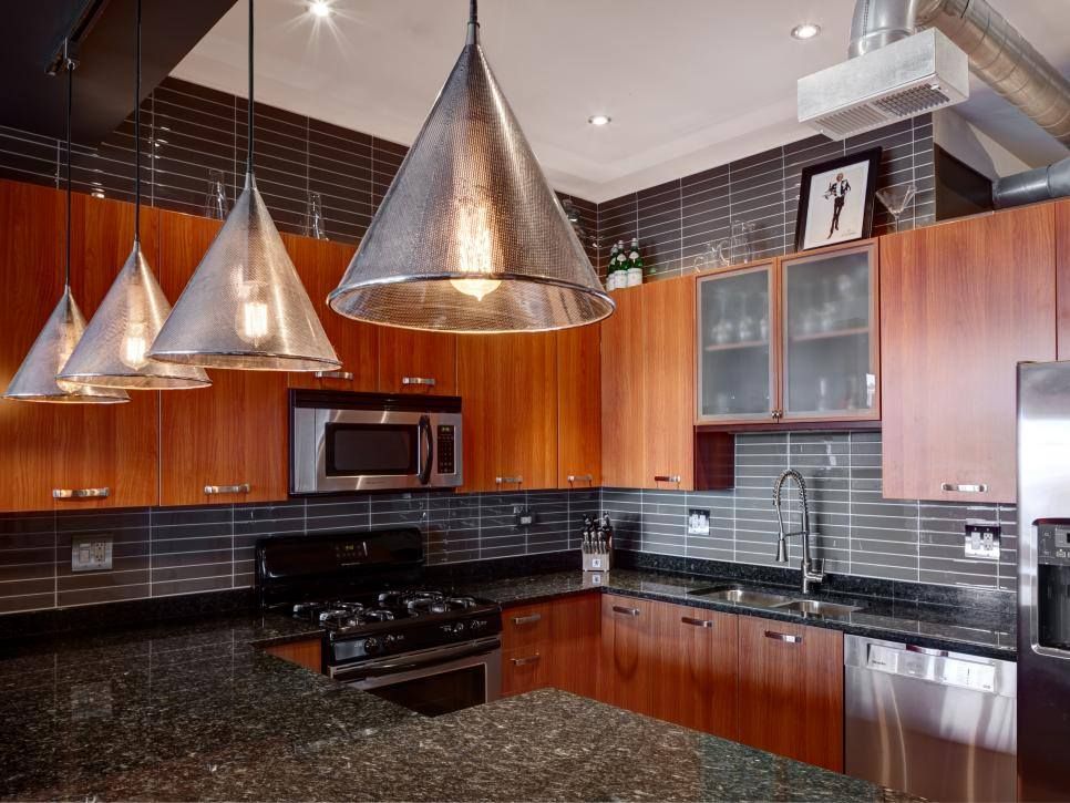 Modern kitchen with wooden cabinets, black countertops, metallic cone pendant lights, and stainless steel appliances.