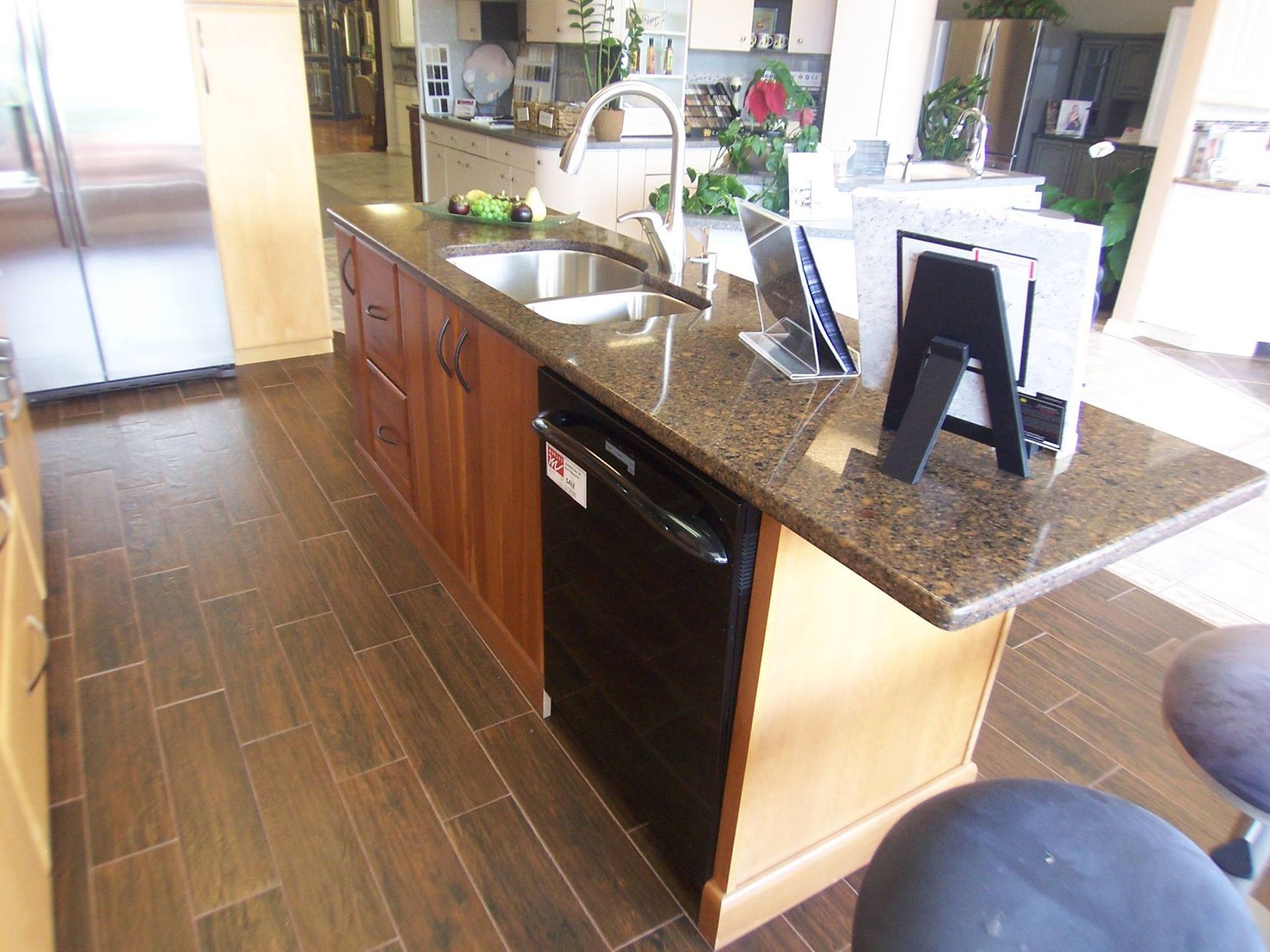 Kitchen island with sink, dishwasher, and granite countertop, brown cabinets, and wooden floor.