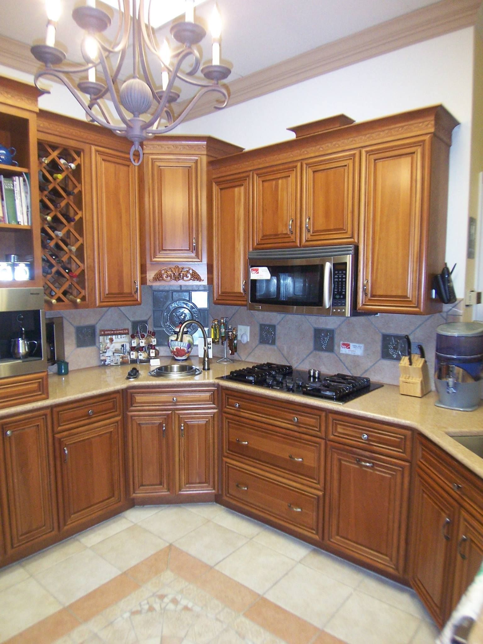 Kitchen with wood cabinets, microwave, stovetop, and wine rack; light-colored countertops and tile backsplash.