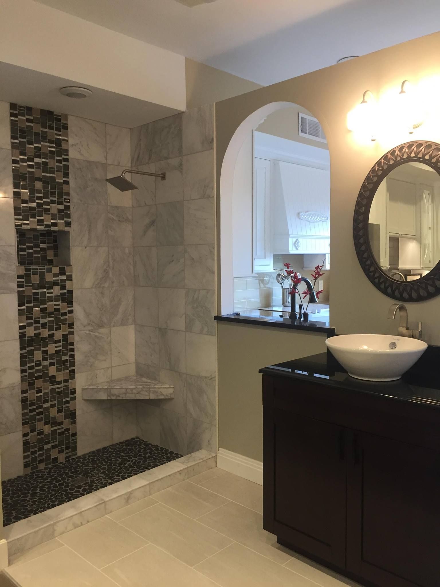 Modern bathroom with tiled shower and sink, neutral colors, dark vanity, and arched opening.