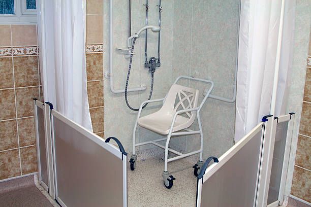 Shower with white walls and curtains, an accessible chair, and hinged panels.