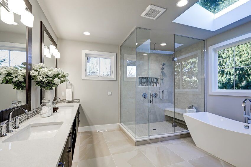 Modern bathroom with glass shower, white tub, and vanity; neutral colors, natural light.