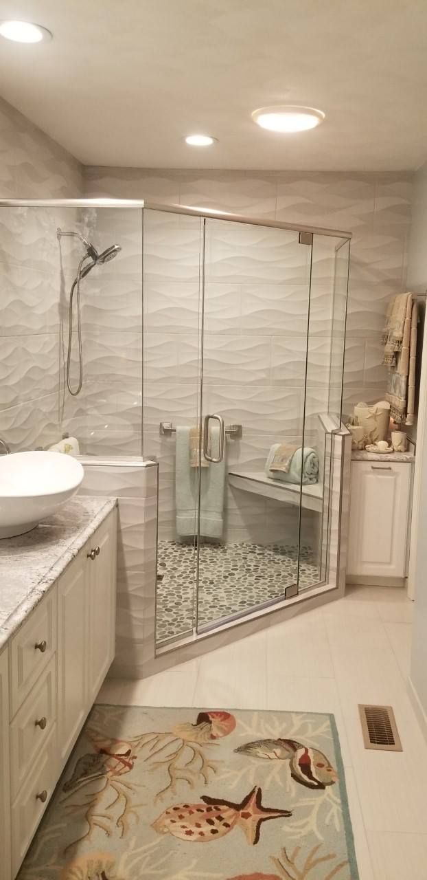 Bathroom with glass shower, stone pebbles, wave-patterned walls, and seashell rug.