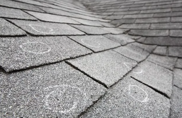 Gray asphalt shingle roof with multiple circular impact marks, likely from hail damage.